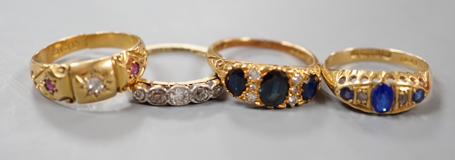 Three early 20th century 18ct and gem set half hoop rings, including ruby and diamond chip, five stone diamond, blue paste and blue stone doublet and diamond chip and a modern 18ct gold sapphire and diamond ring, gross w